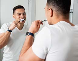 Man brushing teeth while looking in the mirror