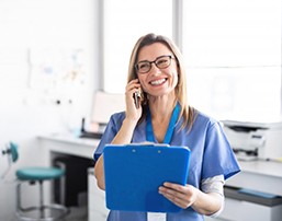 dental team member talking on the phone and holding a clipboard 