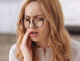 Woman with glasses holding her cheek in pain