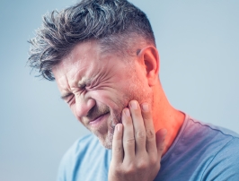 Man in blue shirt holding his jaw in pain
