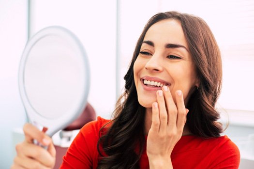 Woman in red-orange shirt touching smile while looking into mirror