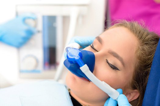 Woman in dental chair with eyes closed and nitrous oxide mask over nose