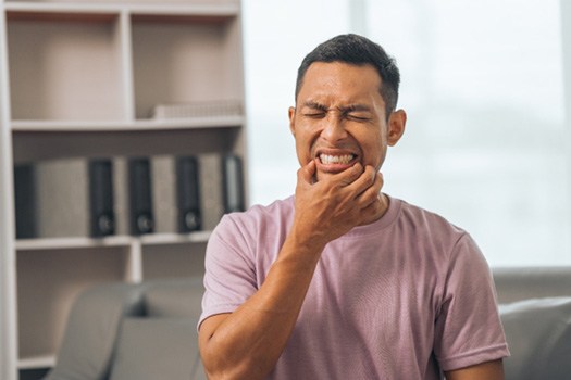 Man in pink shirt squinting in pain and touching corners of his lips with fingers