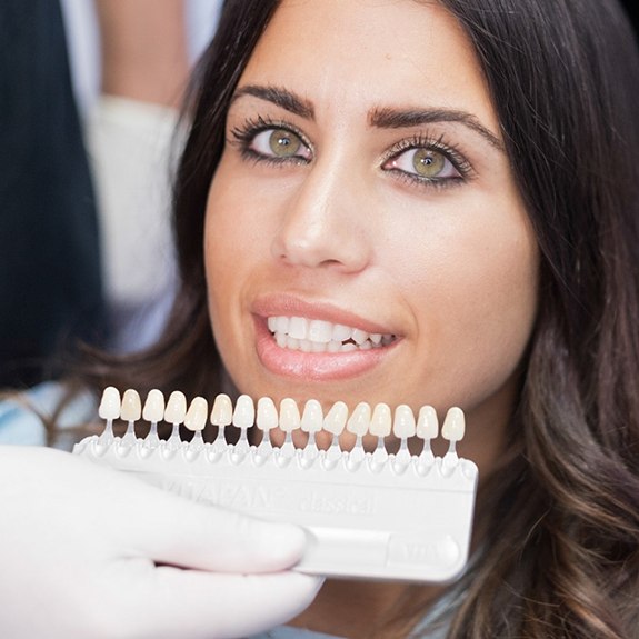 Dentist helping a patient compare veneers to her natural teeth