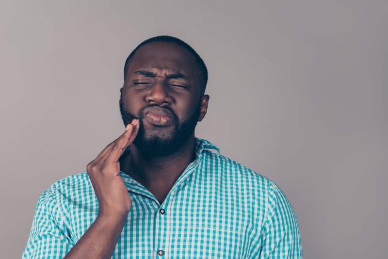 Man in teal gingham button up holding right hand to his cheek while grimacing