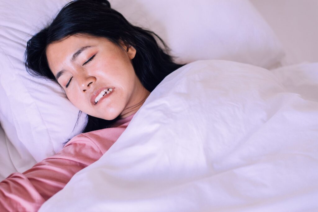 Woman in bed with white covers clenching her teeth